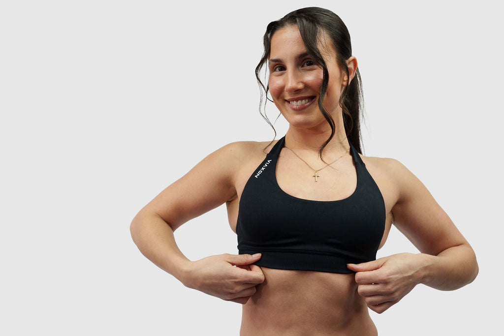 NOXVIA black halter sports bra, front detail showing the supportive underband, scoop neckline and NOXVIA shoulder branding
