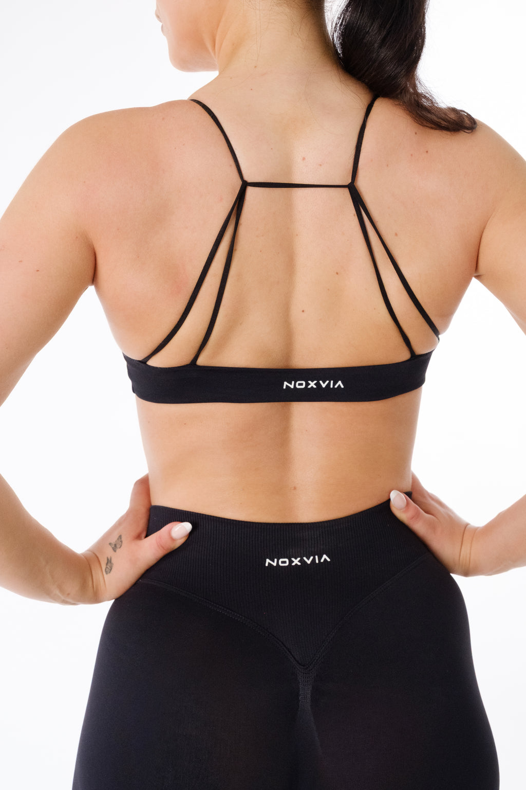 Rear close-up of NOXVIA IMPERIUM black strappy sports bra with matching high-waisted sculpt leggings and logo detail